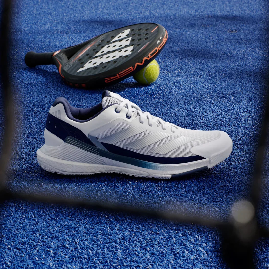 Adidas Crazyquick Boost men's padel shoes (White/Dark Blue) - side view on a blue padel court with a racket and ball